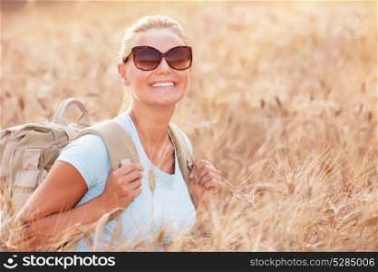 Portrait of cheerful smiling woman sitting in beautiful golden wheat field, travel with backpack along Europe, active lifestyle concept