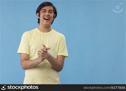 Portrait of cheerful teenage boy clapping against blue background