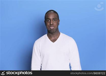 Portrait of cheerful young african-american guy wearing white casual sweater posing isolated on blue background. Carefree young millennial man looking at camera and laughing