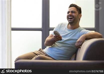 Portrait of cheerful young man watching television while sitting on sofa in living room