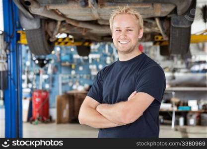 Portrait of cheerful young mechanic with arms crossed standing in his auto repair shop