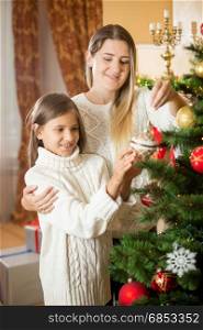 Portrait of cheerful young mother decorating Christmas tree with daughter at house
