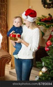 Portrait of cheerful young mother giving present to her baby son on Christmas