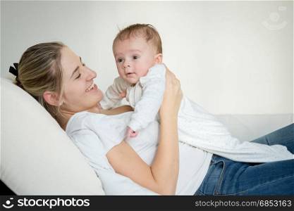 Portrait of cheerful young mother lying with her baby on bed