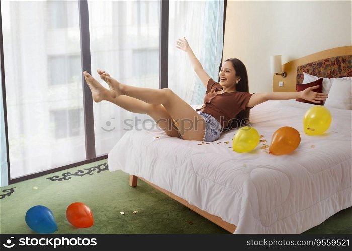 Portrait of cheerful young woman with colourful balloons enjoying on bed