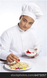 Portrait of chef placing cherry tomato on plate of noodles