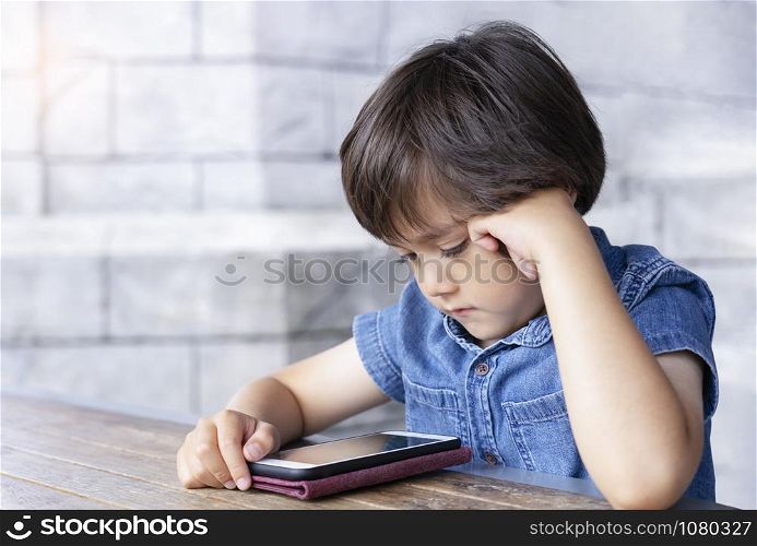 Portrait of Child boy playing playing game on mobile phone, Cute kid sitting outdoor cafe waching cartoons on cell phone while waiting for food. Children with Technology concept.