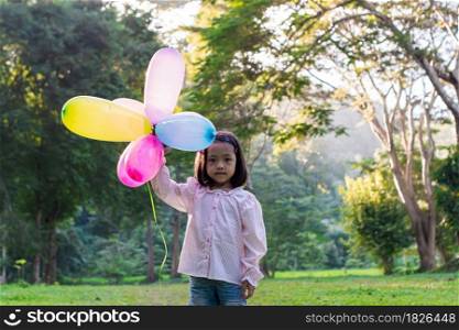 Portrait of child girl holding colorful toy balloons in the park outdoors.