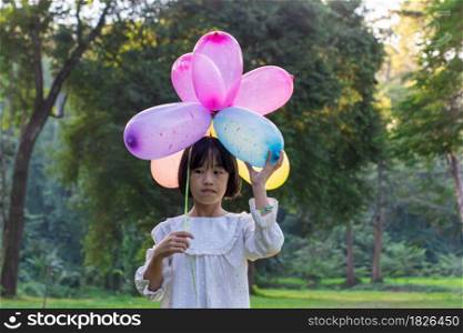 Portrait of child girl holding colorful toy balloons in the park outdoors.