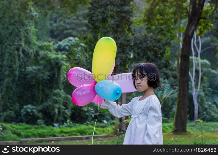 Portrait of child girl holding colorful toy balloons in the park outdoors.