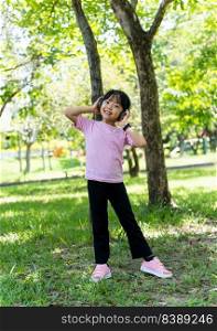 Portrait of child girl listens to music with modern headphones in park outdoors. Happy child enjoying rhythms in listening to music with headphones wireless