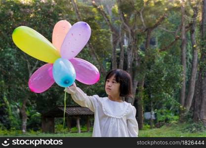 Portrait of child girl playing with colorful toy balloons in the park outdoors.