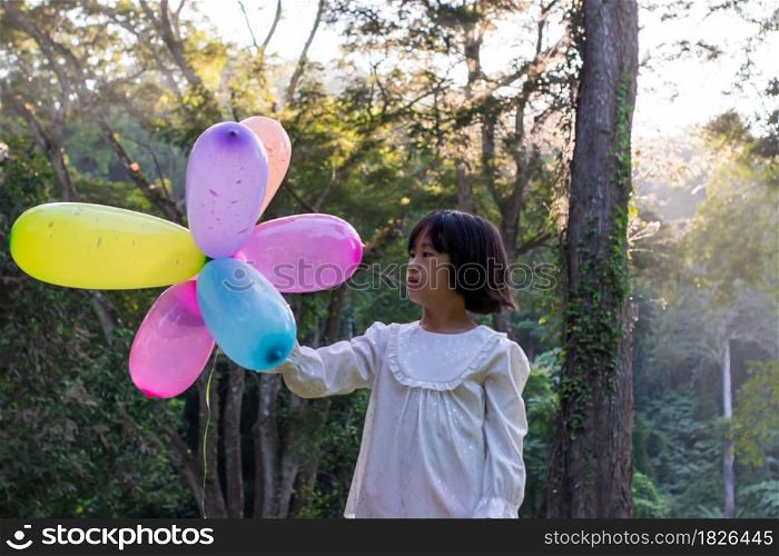 Portrait of child girl playing with colorful toy balloons in the park outdoors.