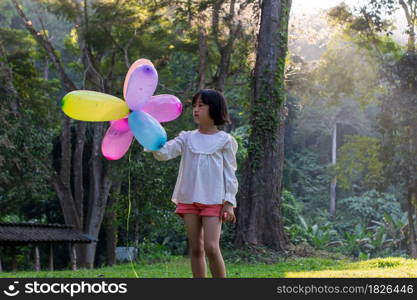 Portrait of child girl playing with colorful toy balloons in the park outdoors.