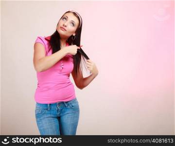 Portrait of childish thoughtful young woman combing her hair and dreaming. Infantile pensive girl with comb on pink. Longing for childhood. Studio shot.