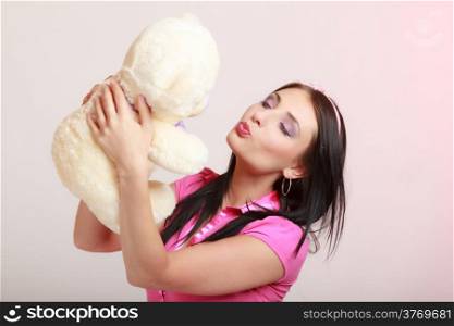 Portrait of childish young woman with headband holding toy. Infantile girl hugging kissing teddy bear on pink. Longing for childhood. Studio shot.