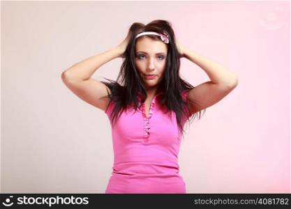 Portrait of childish young woman with headband. Infantile girl messing up her hair on pink. Longing for childhood. Studio shot.