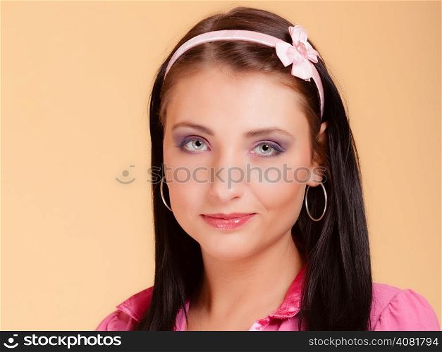 Portrait of childish young woman with headband on her hair. Infantile girl in pink on orange. Longing for childhood. Studio shot.