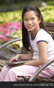 Portrait Of Chinese Girl Sitting On Park Bench With Digital Tablet