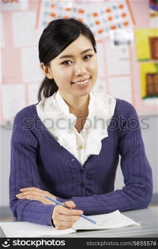 Portrait Of Chinese Teacher Sitting At Desk In School Classroom