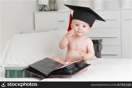Portrait of clever baby boy in graduation cap posing with books