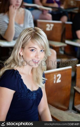 Portrait of college girl sitting in auditorium with classmates in background