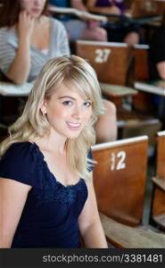 Portrait of college girl sitting in auditorium with classmates in background