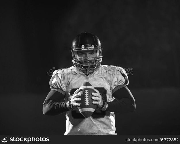 portrait of confident American football player holding ball while standing on field at night