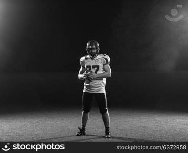 portrait of confident American football player holding ball while standing on field at night