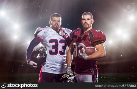 portrait of confident American football players holding ball while standing on big modern american football stadium field with flares and lights