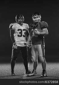 portrait of confident American football players holding ball while standing on field at night