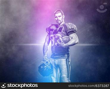 portrait of confident American football players holding ball while standing on the big modern stadium field with lights and flares at night