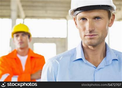 Portrait of confident architect at construction site with coworker in background
