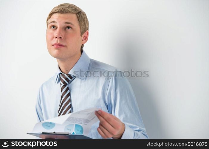 Portrait of confident business man holding document and thinking while leaning on the wall at his office