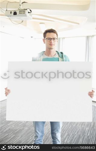Portrait of confident businessman holding blank board in creative office