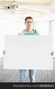 Portrait of confident businessman holding blank board in creative office