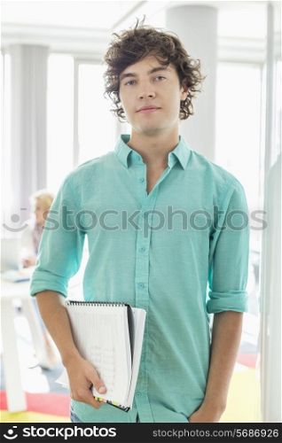 Portrait of confident businessman holding files at creative office