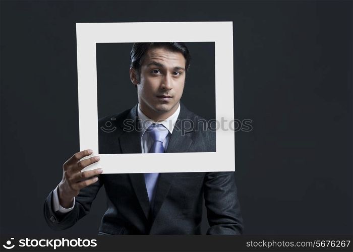 Portrait of confident businessman holding picture frame against black background