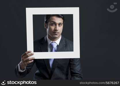 Portrait of confident businessman holding picture frame against black background