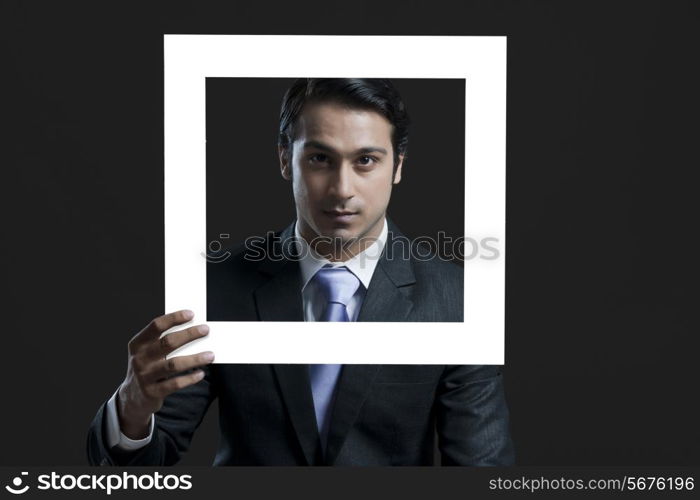 Portrait of confident businessman holding picture frame over black background