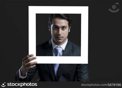 Portrait of confident businessman holding picture frame over black background