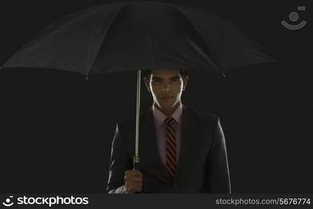 Portrait of confident businessman holding umbrella against black background