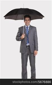 Portrait of confident businessman holding umbrella against gray background