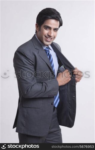 Portrait of confident businessman keeping money in pocket against gray background