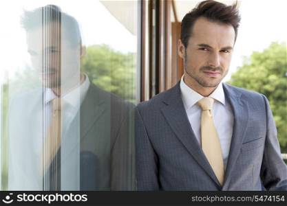 Portrait of confident businessman leaning on glass door
