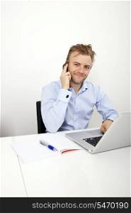Portrait of confident businessman on call while using laptop in office