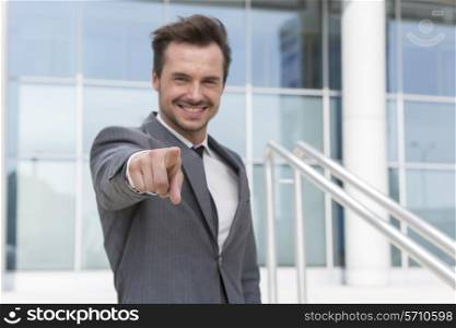 Portrait of confident businessman pointing at you outside office building