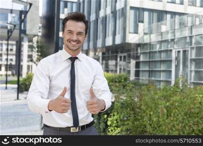 Portrait of confident businessman showing thumbs up outside office building