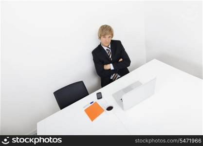 Portrait of confident businessman sitting at desk with laptop