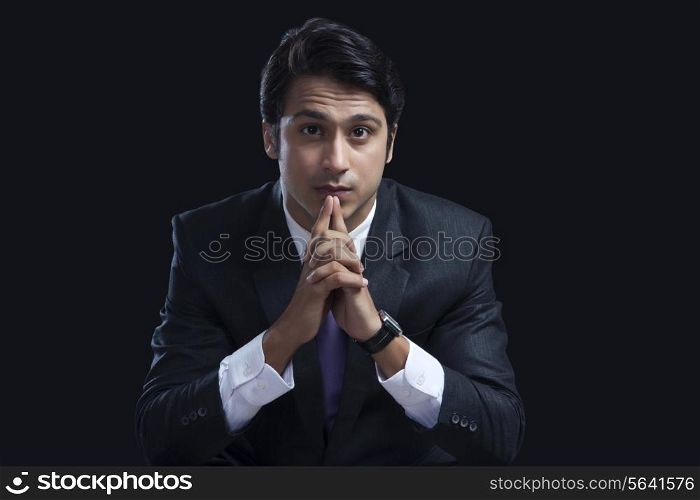 Portrait of confident businessman sitting with hands clasped against black background